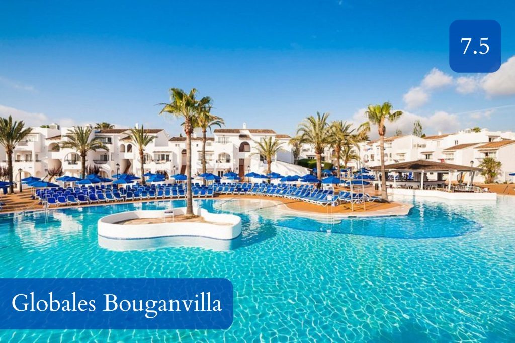 Expansive outdoor swimming pool with a palm tree island, blue sun loungers, and white Mediterranean-style buildings at Globales Bouganvilla near Sa Coma, Mallorca