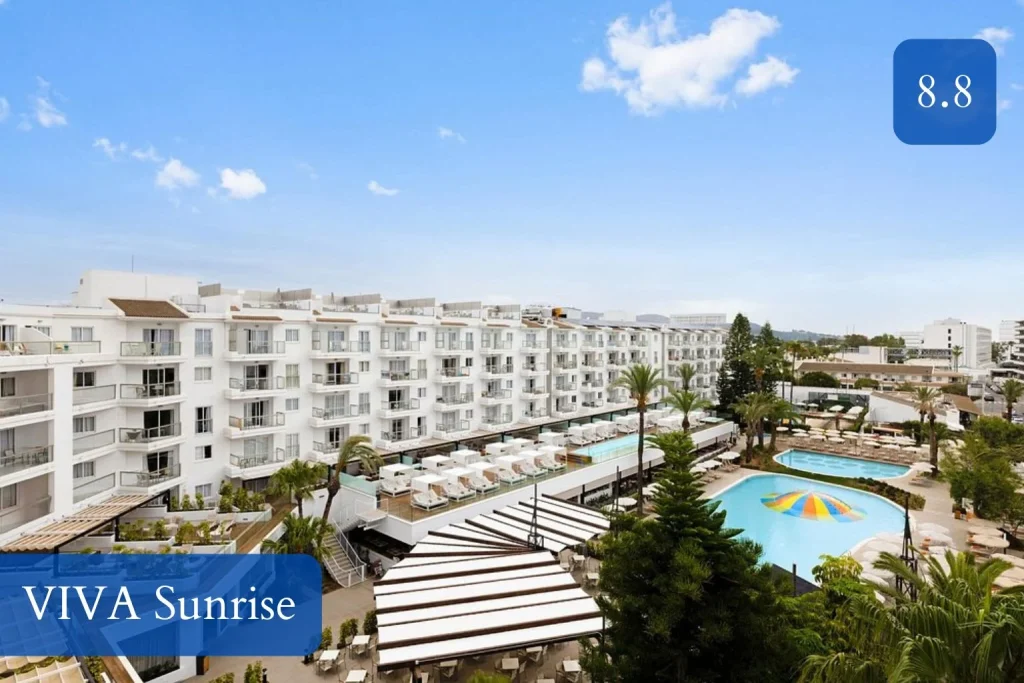 Elevated view of VIVA Sunrise Resort featuring outdoor swimming pools, sun loungers, landscaped gardens, palm trees, and modern apartment-style accommodations in Port d’Alcudia, Mallorca