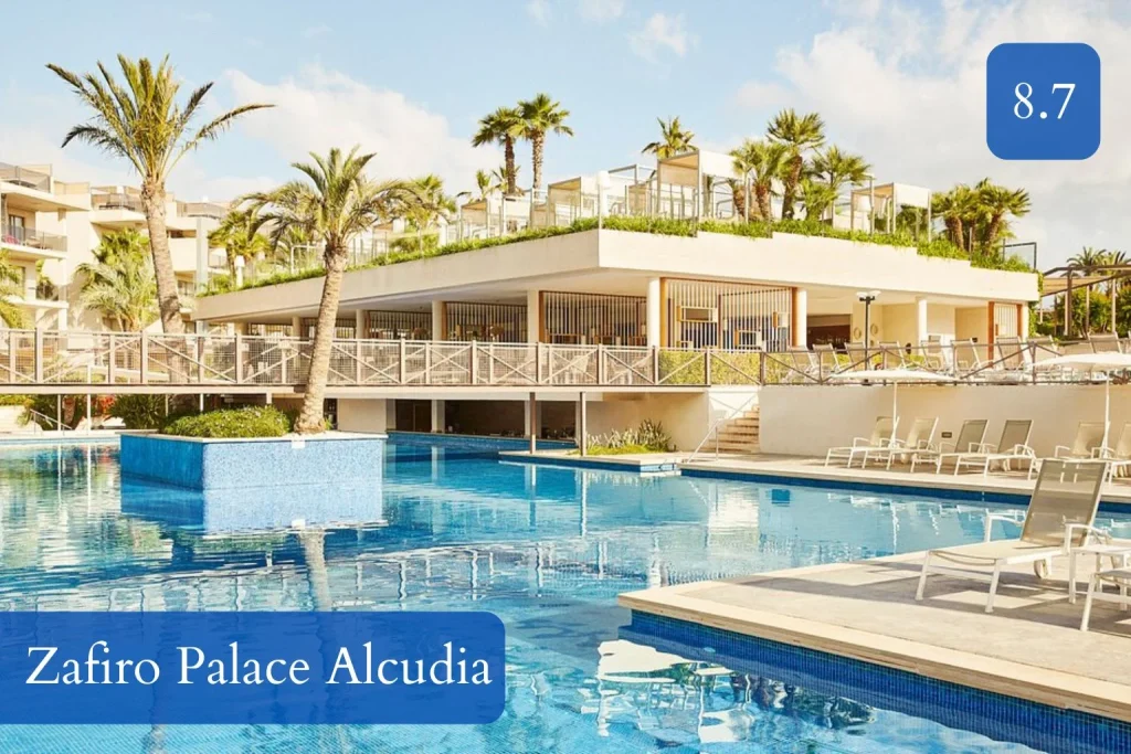 Large outdoor swimming pool with sun loungers and palm trees at Zafiro Palace Alcudia in Port d'Alcudia, Mallorca.