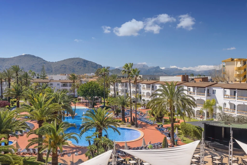 Lagoon-style pools with palm gardens and mountain views at Alcudia Garden Aparthotel in Port d'Alcúdia, Mallorca.