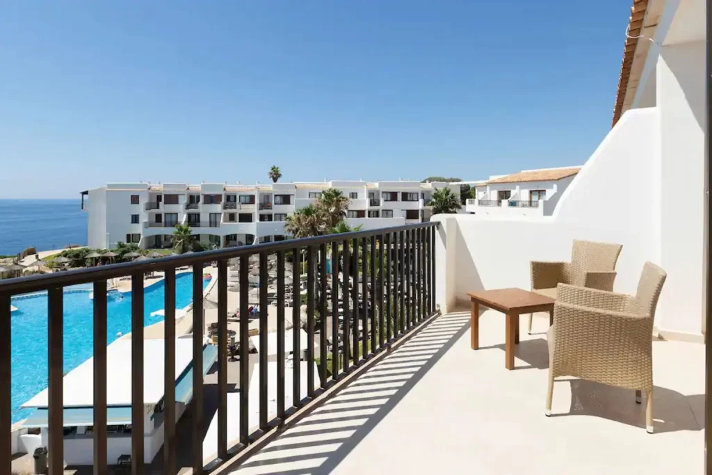 Private balcony overlooking the outdoor swimming pool and Mediterranean Sea at Alua Suites Las Rocas in Cala d'Or, Mallorca.