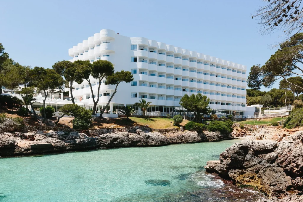 Seafront hotel building overlooking a rocky cove and turquoise water at AluaSoul Mallorca Resort – Adults Only in Cala Egos, Mallorca.