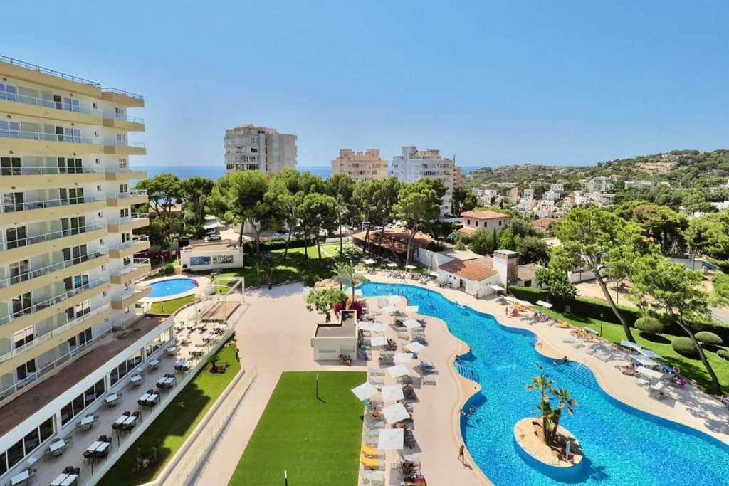 Lagoon-style outdoor swimming pool with island feature, sun loungers, spacious sun terrace, landscaped grounds, and panoramic coastal views at BQ Belvedere Hotel in Mallorca