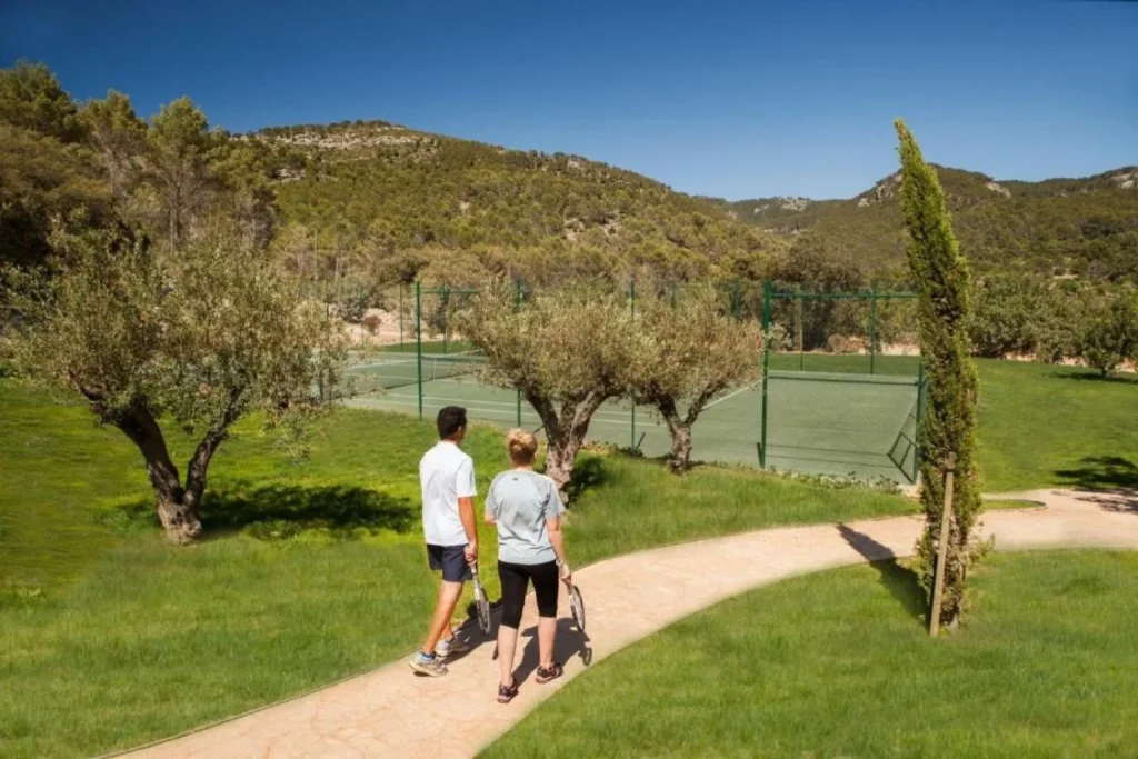 A peaceful walk through the gardens leads to the outdoor tennis court at Castell Son Claret, set among olive groves with beautiful Tramuntana mountain views.