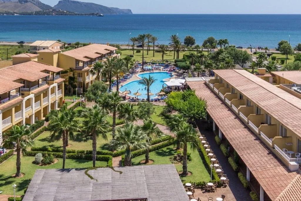 Aerial view of the pool, tropical gardens, and beachfront at Club Del Sol Hotel & Apartments in Port de Pollença.