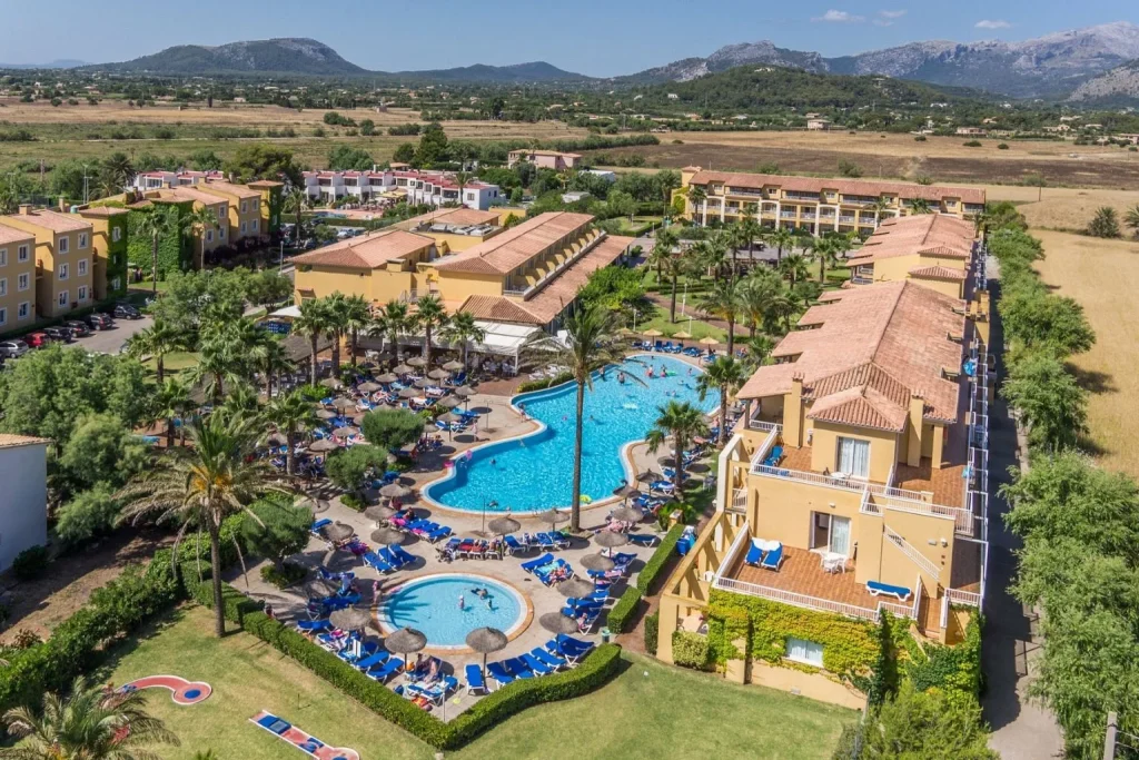 Aerial view of the main lagoon-style swimming pool surrounded by palm trees at Club Del Sol Hotel & Apartments in Puerto Pollensa, Majorca.