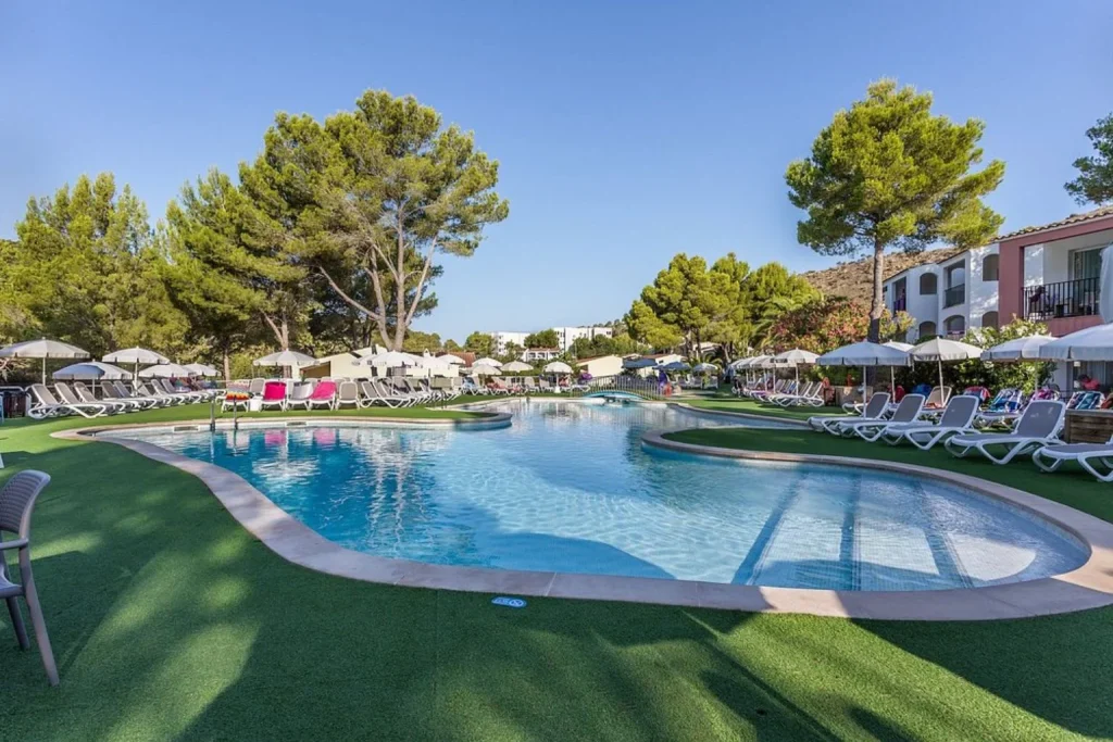 Lagoon-style outdoor swimming pool surrounded by sun loungers and pine trees at FERGUS Club Europa in Peguera, Majorca.