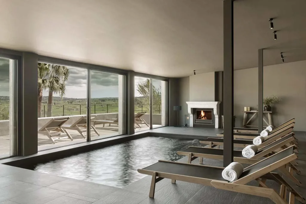 Indoor relaxation pool with lounge chairs, fireplace, and countryside views at Único Spa in Finca Serena, Montuïri, Mallorca.