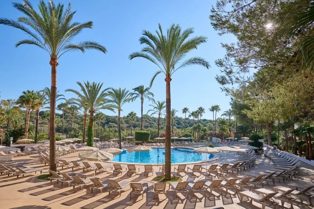 Main swimming pool surrounded by palm trees and gardens at Grupotel Cala Marsal Natura Hotel near Cala Marsal.
