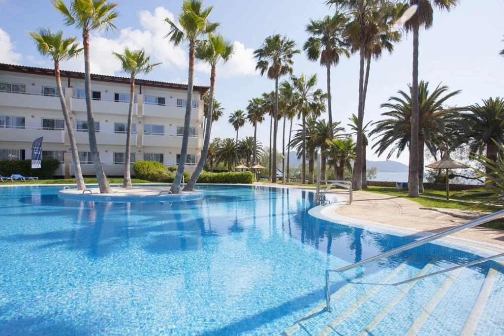 Large outdoor swimming pool surrounded by palm trees and gardens at Grupotel Mallorca Mar in Cala Bona, Mallorca.
