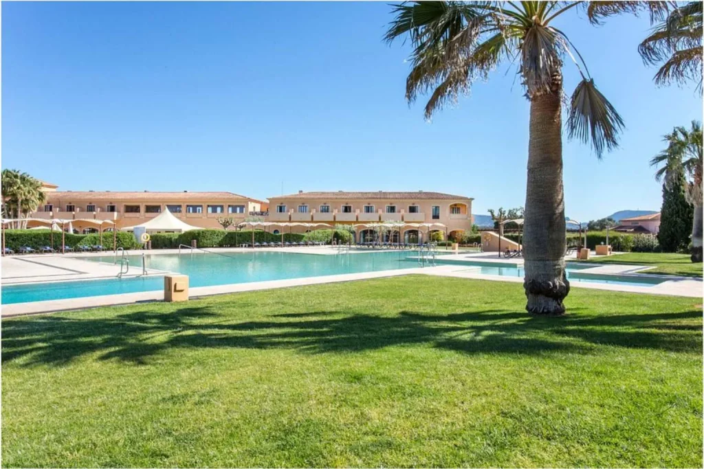 Large outdoor swimming pool surrounded by palm trees, landscaped gardens, and resort buildings at Hacienda Son Antem Golf Resort in Llucmajor, Mallorca.