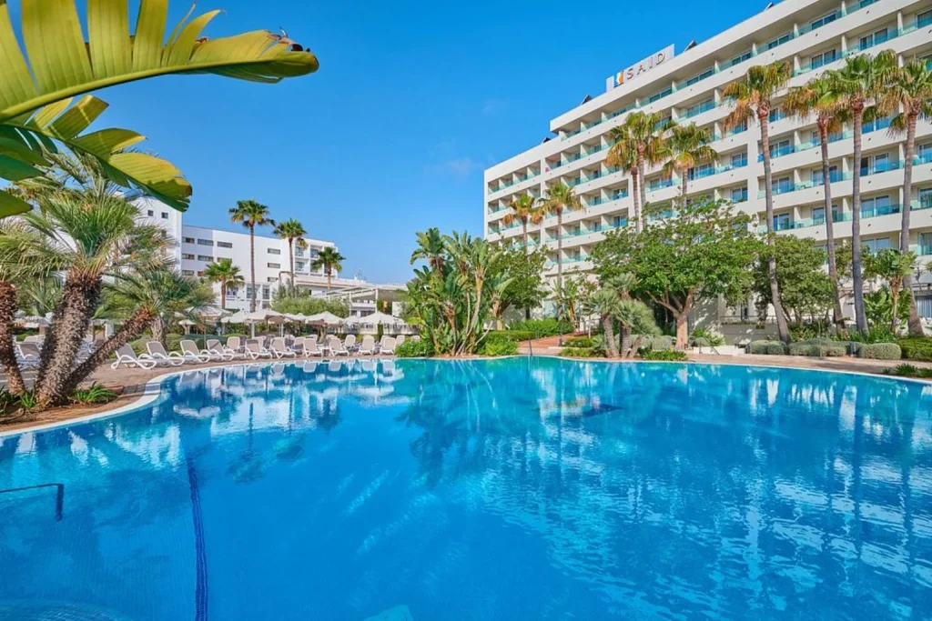 Large outdoor swimming pool surrounded by palm trees at Hipotels Said in Cala Millor, Majorca.