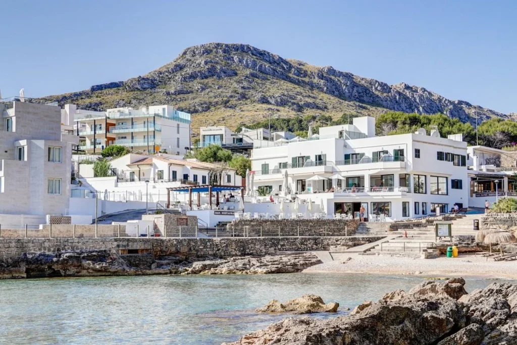 Seafront hotel exterior with mountain backdrop at Hoposa Niu in Cala Sant Vicenç, Mallorca