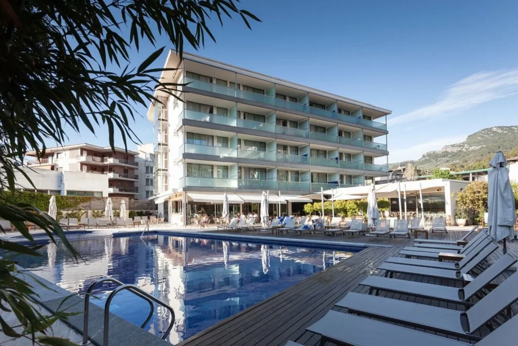 Outdoor swimming pool with a sun terrace, loungers, and modern hotel façade at Hotel Aimia in Port de Sóller, Mallorca.