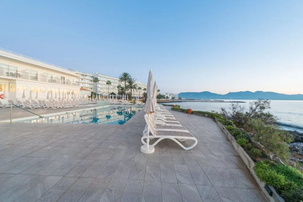 Seafront swimming pool with sun loungers overlooking the Mediterranean Sea at Hotel Atolon & Kaafu Beach Club in Cala Bona, Mallorca.