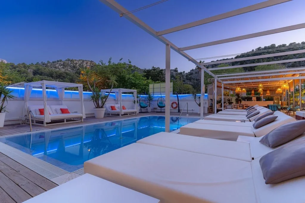 Evening view of the outdoor swimming pool with daybeds, private cabanas, and lounge area at Hotel Boutique Minister in Port de Sóller, Mallorca