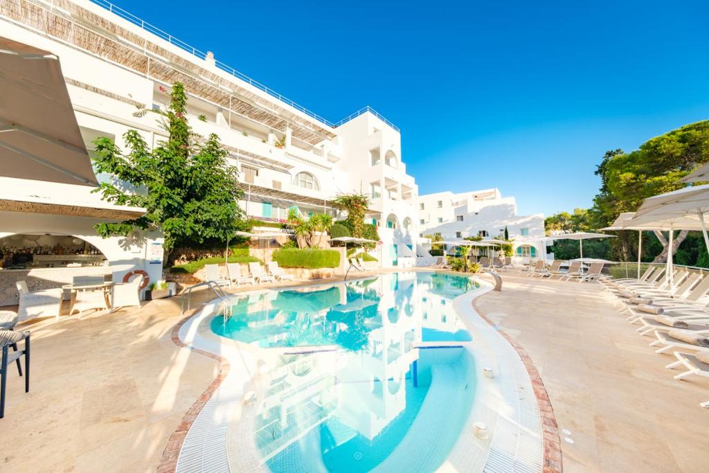 Outdoor swimming pool and white Mediterranean-style hotel buildings at Hotel Cala d'Or in Cala d'Or, Mallorca.