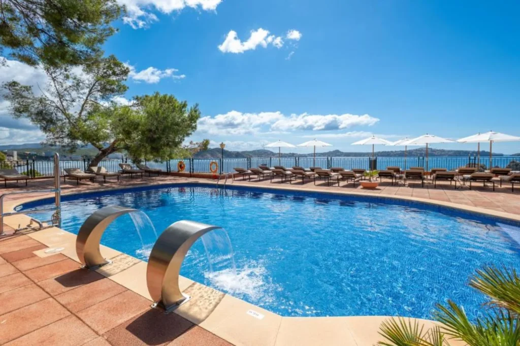 Outdoor swimming pool with waterfall features and sea views at Hotel Cala Fornells in Peguera, Majorca.