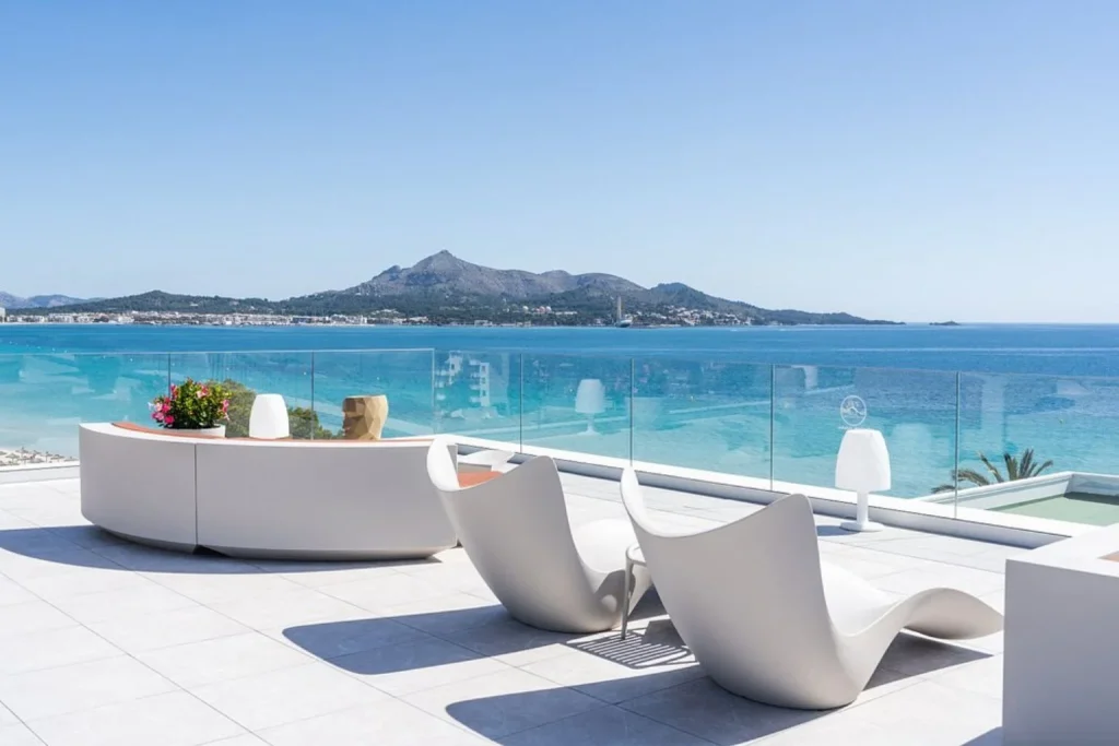 Modern rooftop terrace with designer lounge seating, glass railing, panoramic Alcudia Bay views, and mountain backdrop at Hotel Condesa in Mallorca
