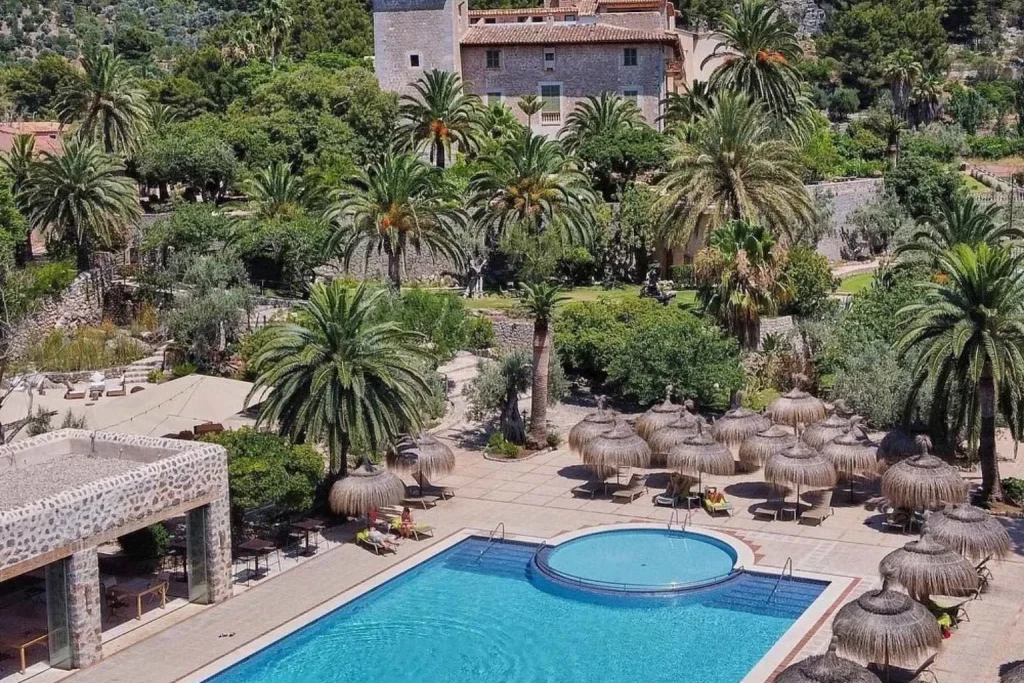 Large outdoor swimming pool surrounded by palm trees, gardens, and mountain scenery at Hotel Es Port in Port de Sóller, Mallorca.