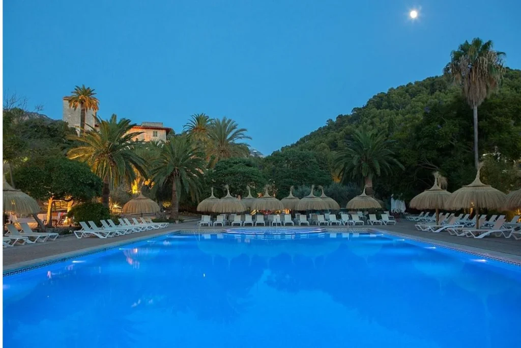 Outdoor swimming pool with sun loungers, palm trees, and surrounding hills at Hotel Es Port in Port de Sóller, Mallorca