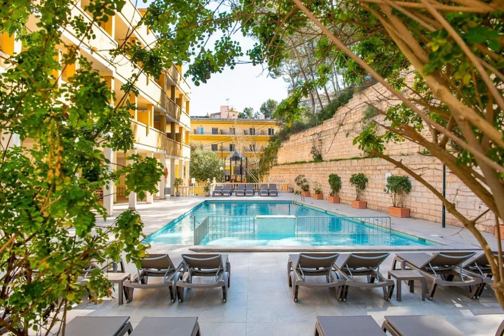 Outdoor swimming pool with sun loungers and landscaped courtyard at Hotel Flor Los Almendros in Peguera, Majorca.