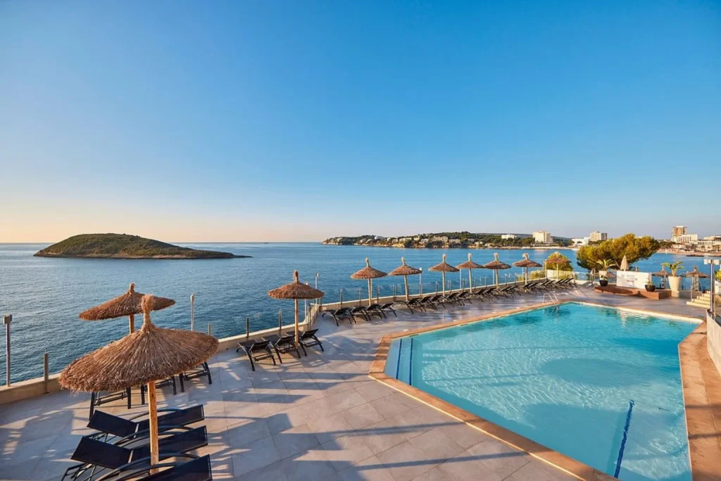 Oceanfront swimming pool with sun loungers and parasols overlooking the Mediterranean Sea at Hotel Florida Magaluf in Mallorca.