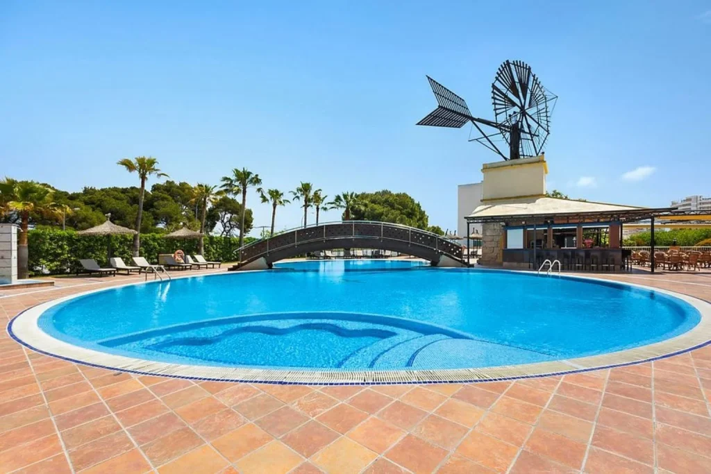 Round outdoor swimming pool with a wooden bridge, pool bar, palm trees, and sun loungers at Hotel THB El Cid in Can Pastilla, Mallorca