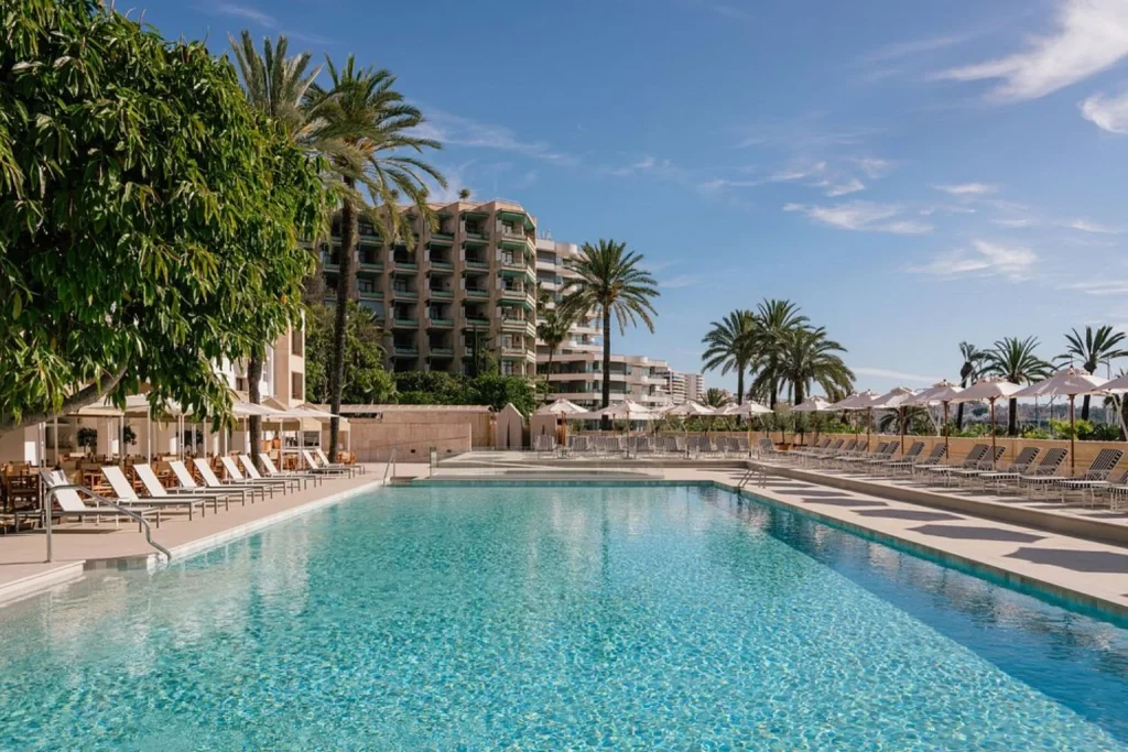 Large outdoor swimming pool surrounded by palm trees, sun loungers, and parasols at Hotel Victoria Gran Meliá in Palma, Mallorca