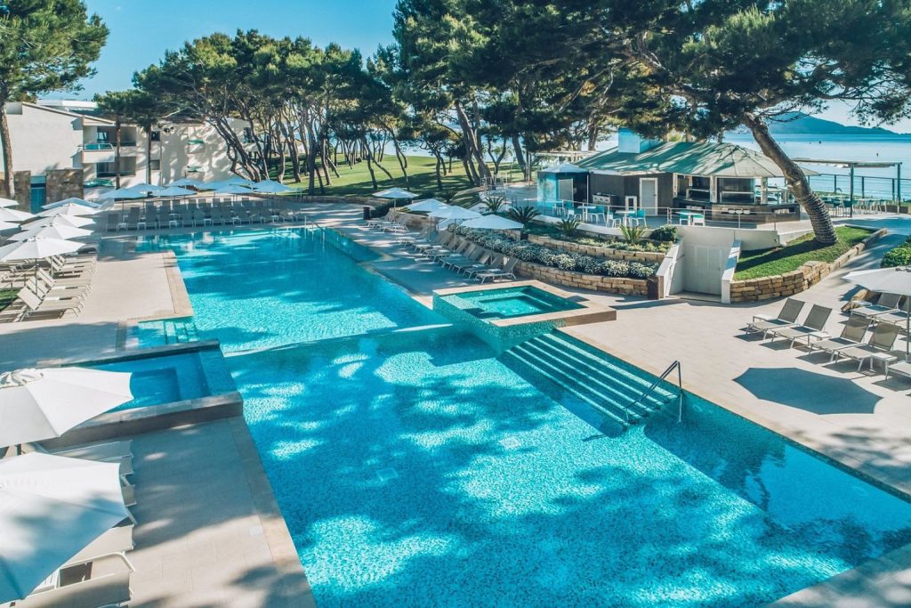 Luxury outdoor swimming pool with shallow entry steps, integrated whirlpool, sun loungers, poolside restaurant, and beachfront setting at Iberostar Selection Playa de Muro Village in Mallorca