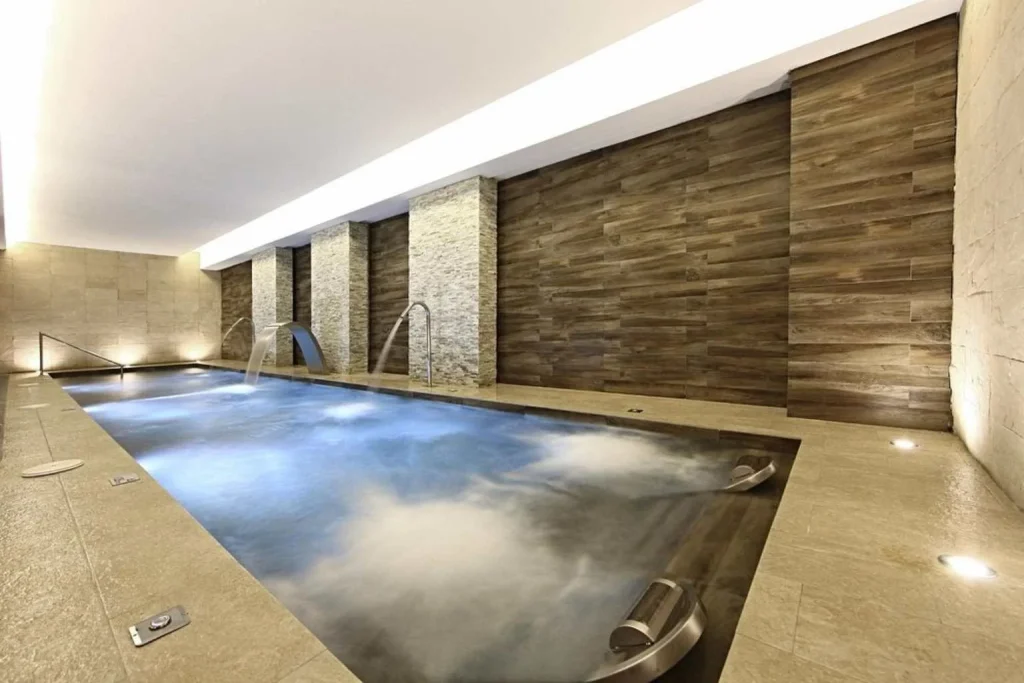 Indoor hydrotherapy pool with massage jets, waterfall features, and contemporary stone-and-wood design at Iberostar Waves Cala Millor, Mallorca.