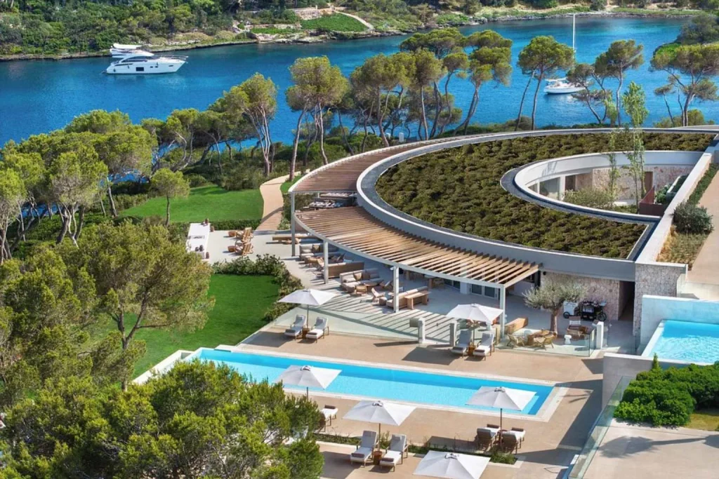 Aerial view of the main infinity pool, waterfront setting, and contemporary architecture at Ikos Porto Petro in Porto Petro, Mallorca.