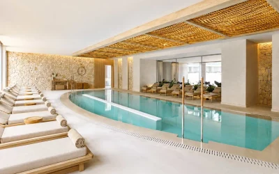 The indoor spa at Ikos Porto Petro features a serene heated pool, elegant relaxation loungers, and a contemporary wellness space with natural Mediterranean-inspired design.