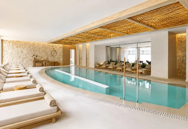The indoor spa at Ikos Porto Petro features a serene heated pool, elegant relaxation loungers, and a contemporary wellness space with natural Mediterranean-inspired design.