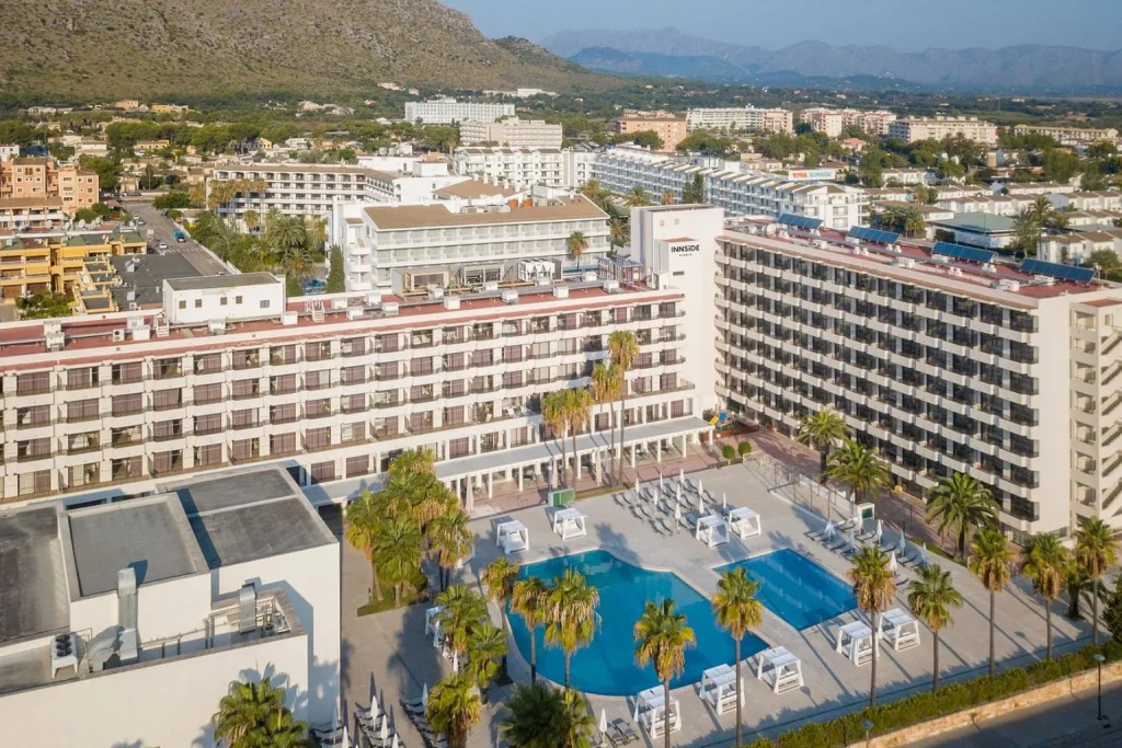 Aerial view of the outdoor swimming pool and modern hotel building at INNSiDE by Meliá Alcudia in Port d'Alcúdia, Majorca.