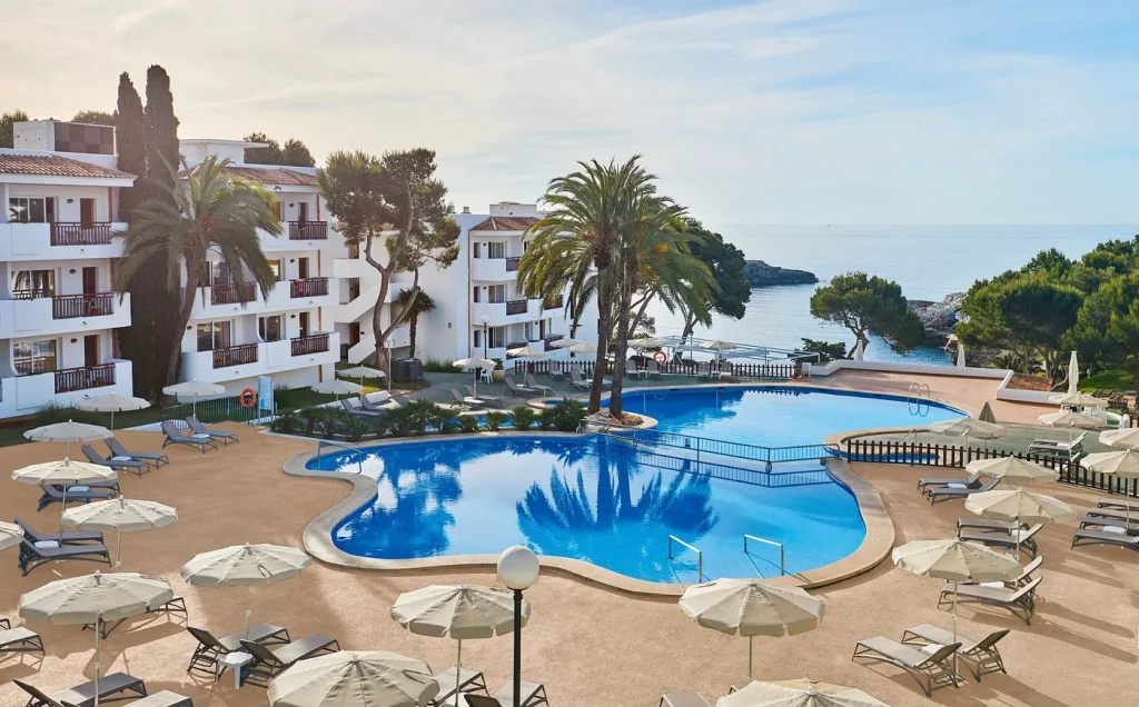 Seafront swimming pool with palm trees and sun loungers at Inturotel Cala Azul in Cala d'Or, Mallorca.
