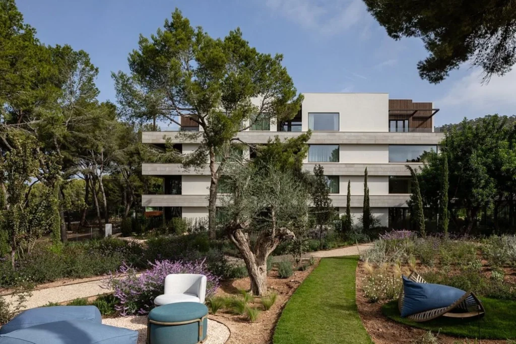 Modern hotel building surrounded by landscaped Mediterranean gardens at Kimpton Aysla Mallorca in Santa Ponsa.