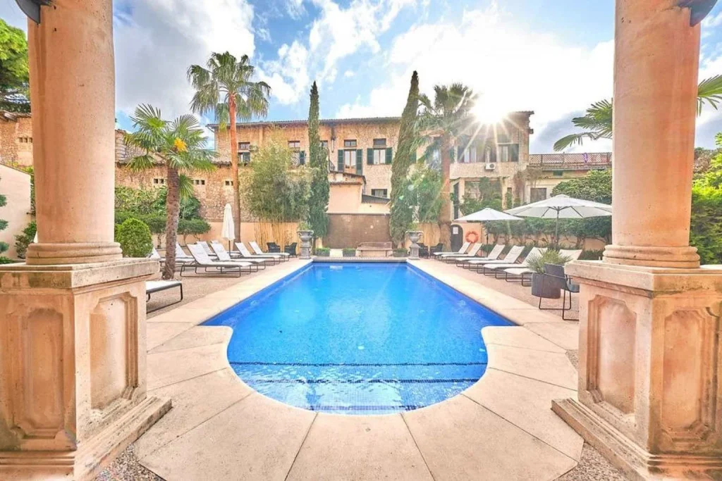 Elegant outdoor swimming pool framed by historic stone architecture and palm trees at L'Avenida Adults Only in Sóller, Mallorca.