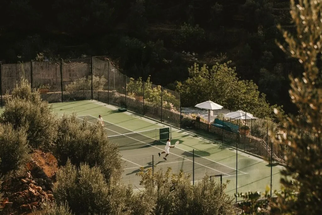 Tennis court surrounded by olive trees and the Tramuntana mountains at La Residencia in Deià.