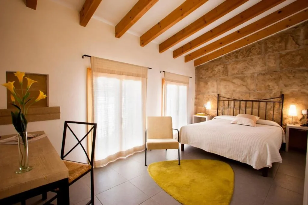 Double guest room with exposed stone wall and wooden ceiling beams at L'Host Boutique Rooms in Pollença Town.