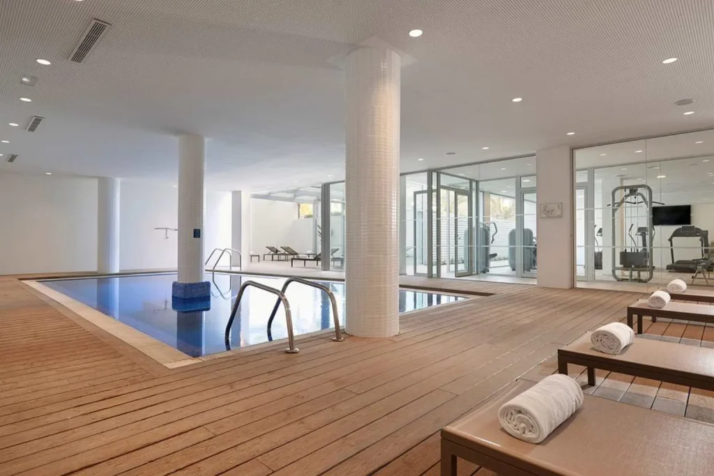 Bright indoor spa pool with wooden deck, sun loungers, and adjacent fitness area at Meliá Calviá Beach in Calvià, Mallorca.