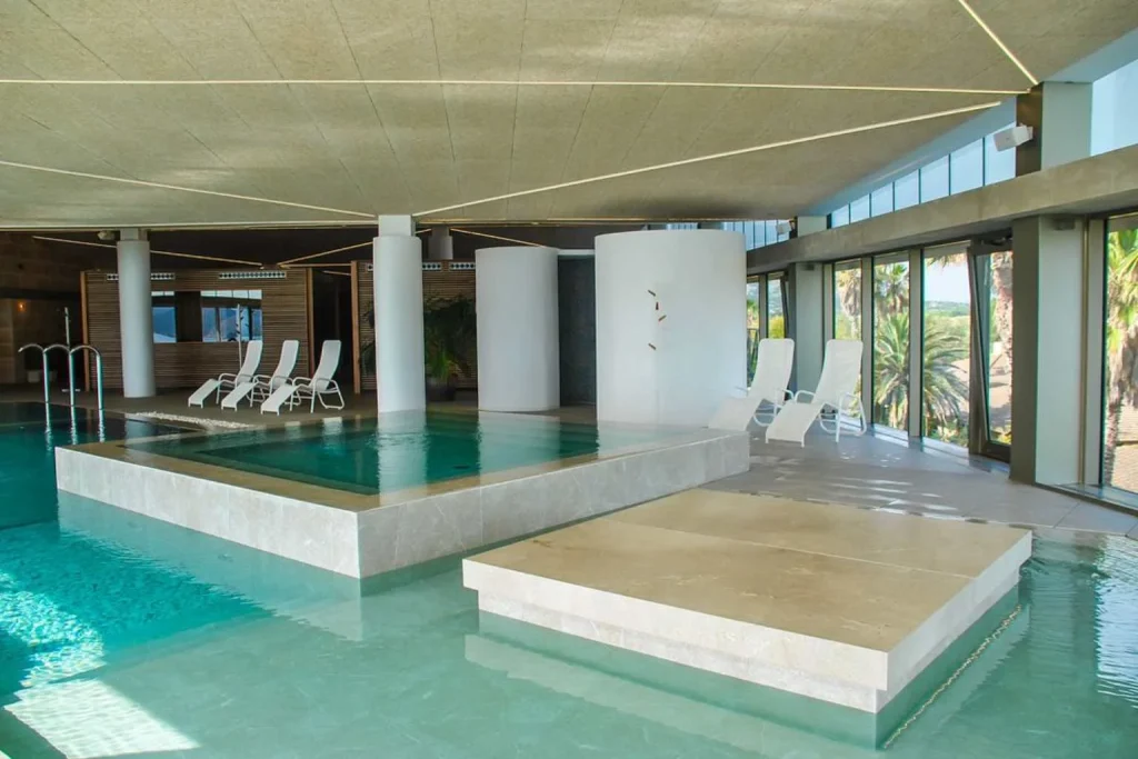 The indoor spa at PortBlue Club Pollentia Resort & Spa features a contemporary heated pool, relaxation areas, and panoramic windows overlooking the resort's palm-filled surroundings.