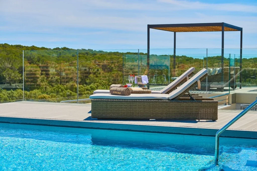 Rooftop infinity pool with luxury daybeds, glass-panel railing, shaded cabana, and panoramic countryside views at Protur Biomar Sensatori Resort in Mallorca