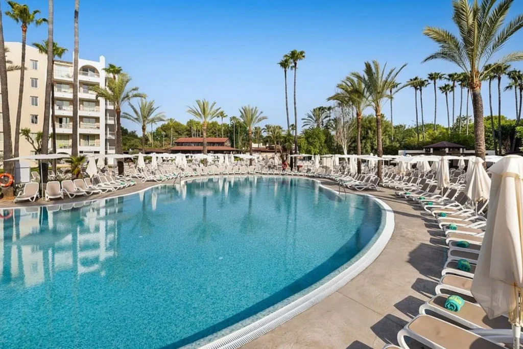 Main outdoor swimming pool surrounded by palm trees and sun loungers at Protur Safari Park Aparthotel in Sa Coma, Mallorca.