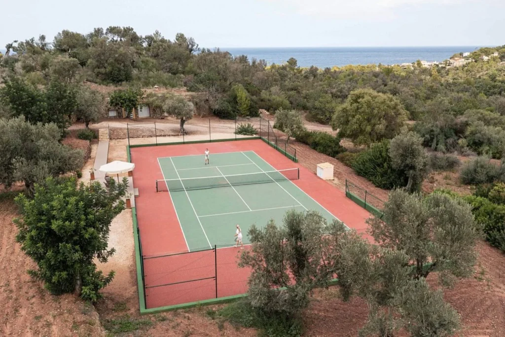 Outdoor tennis court at Son Bunyola in Mallorca surrounded by olive trees, countryside, and distant Mediterranean Sea views.