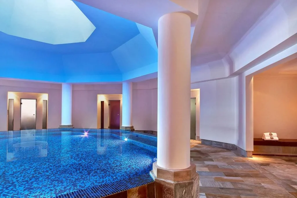 Indoor spa pool with mosaic tiles, ambient blue lighting, and wellness facilities at The St. Regis Mardavall Mallorca Resort in Costa d'en Blanes.