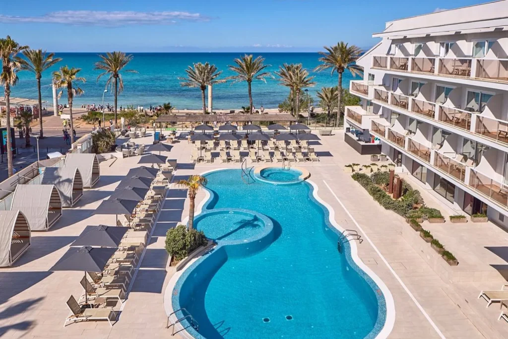 Oceanfront outdoor swimming pool with sun loungers overlooking Playa de Palma Beach at Universal Hotel Neptuno in Playa de Palma, Mallorca.