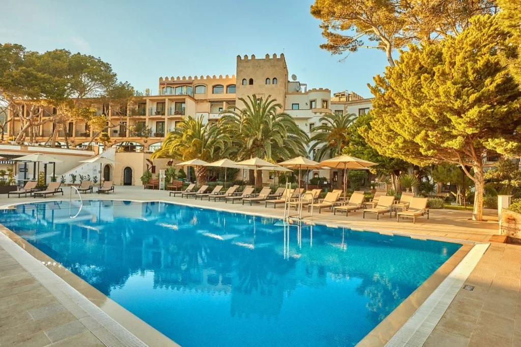 Outdoor swimming pool surrounded by palm trees and sun loungers at Villamil Hotel in Paguera.