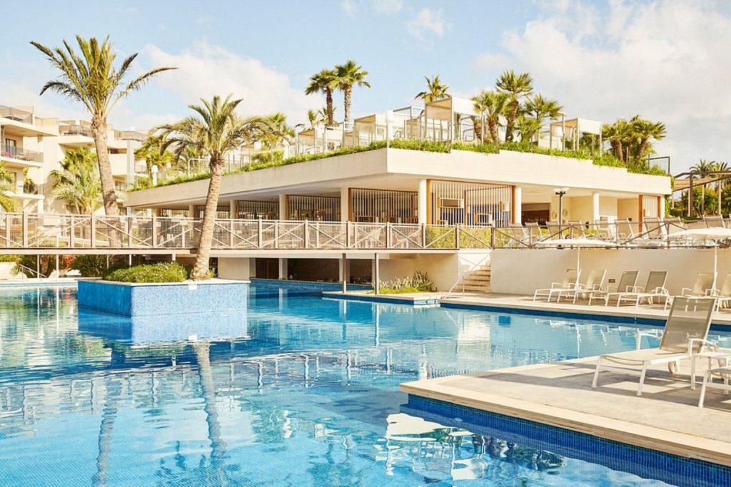Luxury outdoor swimming pool with island planters, pedestrian bridge, spacious sun terrace, modern resort buildings, and premium leisure facilities at Zafiro Palace Alcudia in Mallorca